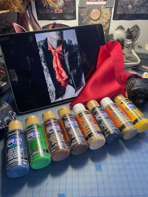 bottles of paint lined up with a scrap of red silk and photo of iii from Sleep Token