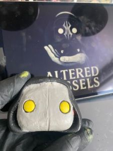 playing with the eyeholes in a layer of clay over the face of a pop vinyl being transformed into a custom Sleep token figurine.