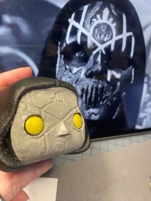 roughing in shapes in a layer of clay over the face of a pop vinyl being transformed into a custom Sleep token figurine.