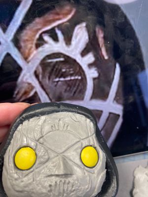 carving the sleep token sigil in a layer of clay over the face of a pop vinyl being transformed into a custom Sleep token figurine.