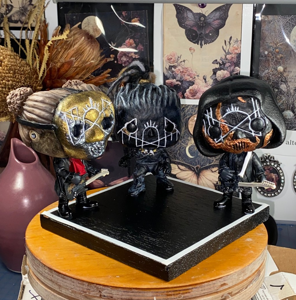 three custom Sleep Token figurines on a band stand